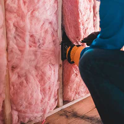 Close up of a worker installing pink insulation on a wall