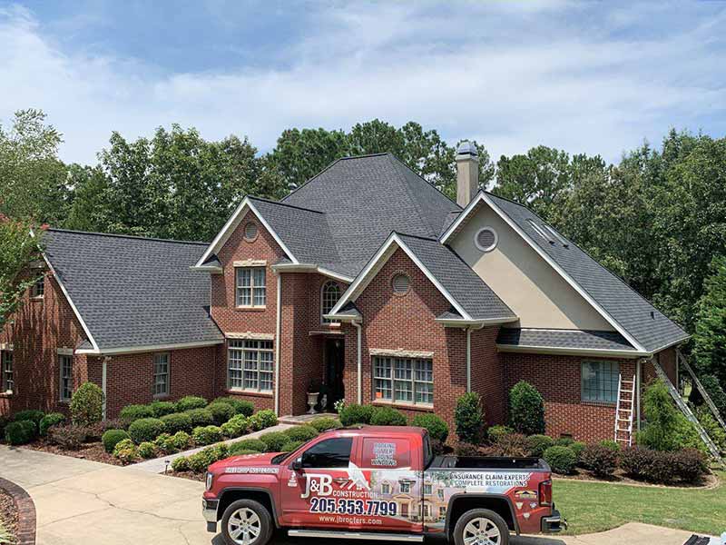 J & B Construction, LLC work pickup in front of a large home with new gray shingles installed by the team