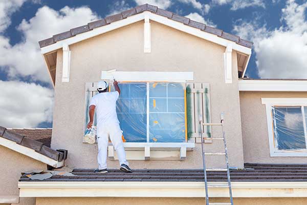 Worker painting the trim around the exterior window of a home