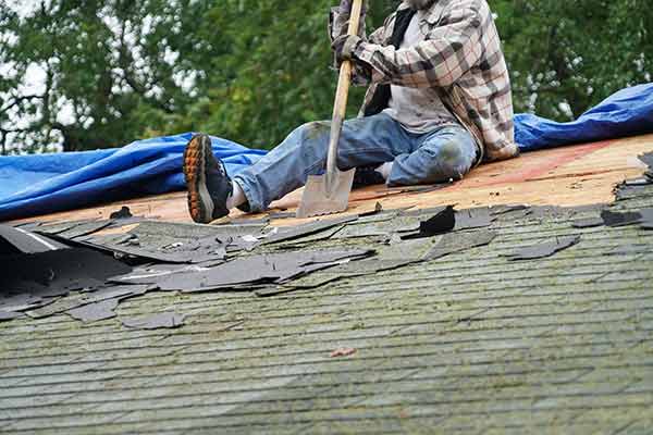 Worker removing old, moldy shingles from a roof with a shovel